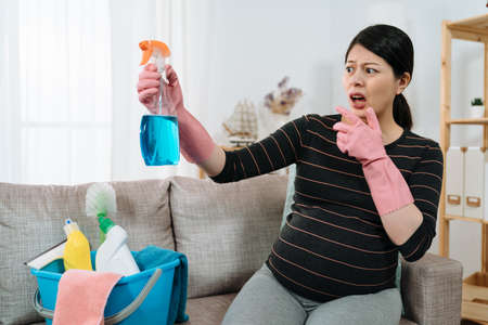 portrait asian expectant housewife with hand near mouth is feeling shocked for finding toxic chemicals while reading the label on the cleanser bottle at home.の写真素材