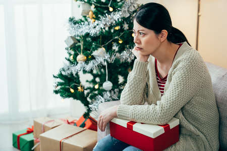 chinese female sitting in sulky silence with a box is unhappy with the cheap Christmas present she got. asian girl is looking away in anger for her boyfriend didnât spend time with her on the holidayの写真素材