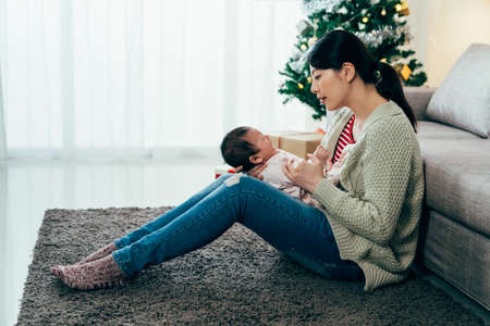 full length asian millennial mom sitting on rug is coaxing her child with verbal soothing. japanese...