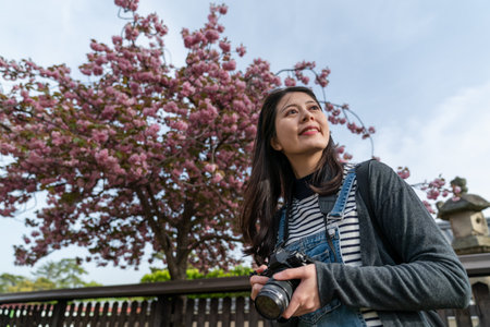 low angle shot of cheerful asian Chinese female photographer enjoying landscape at a Japanese garden with cherry blossom while visiting Kofuku-ji temple in nara japanの写真素材