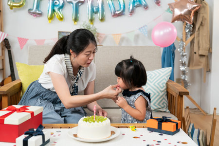 closeup view of cute asian baby girl trying to blow the party horn her mother is holding for her on the birthday celebration at homeの写真素材
