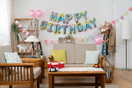 bright living room decorated with colorful birthday party garland, pink balloons and star on white wall and presents on the table. birthday celebration at homeの写真素材