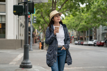 smiling asian chinese girl traveler taking a stroll with coffee on street and looking around surroundings while exploring downtown area in palo alto city California usaの写真素材