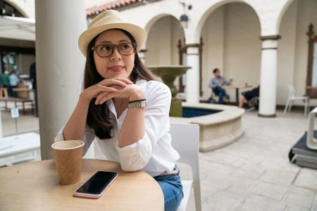 smiling asian Korean woman traveler propping head and looking into space while relaxing in an exotic cafe restaurant in downtown palo alto city California usaの写真素材