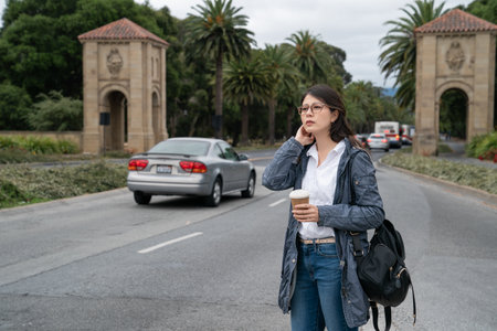 confused asian Korean international girl student looking into distance with coffee and wondering how to get to her classroom at the entrance of Stanford university in California usaの写真素材