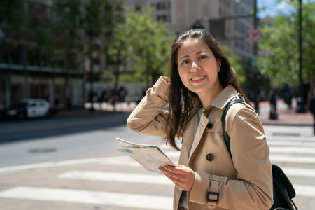 portrait of happy asian Japanese female traveler looking at camera with smiling face and guide map by zebra crossing on street in the sun in san Francisco California usaの写真素材