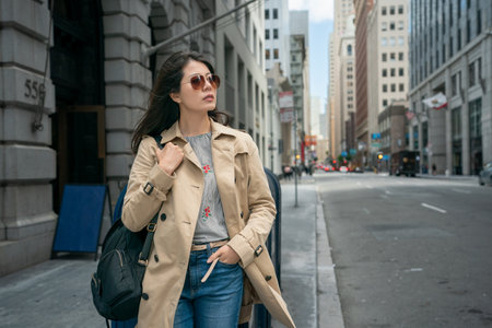 asian Chinese female business woman looking into space with hand in pocket while taking leisure walk on street among tall buildings in city urban san Francisco California usaの写真素材