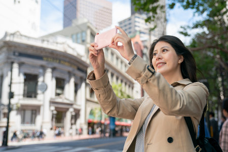 happy asian Japanese female tourist taking picture of the beautiful city with her mobile phone on the corner of street in san Francisco California usaの写真素材