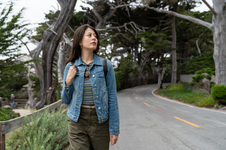 stylish asian Korean girl taking California road trip in united states. she looks up at cypress...