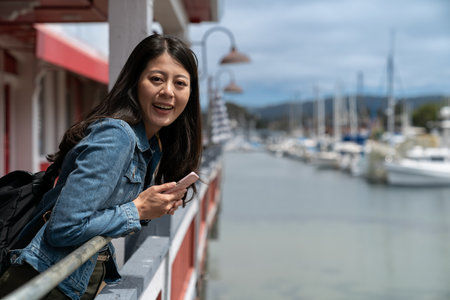 travel lifestyle and people on vacation in usa. portrait of pretty asian woman leaning against waterfront railing and smiling at camera while visiting Old Fisherman's Wharf in Californiaの写真素材