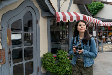 happy asian woman photographer standing near the entrance door of a storybook like restaurant while enjoying scenic streetscape in Carmel by the sea California usaの写真素材