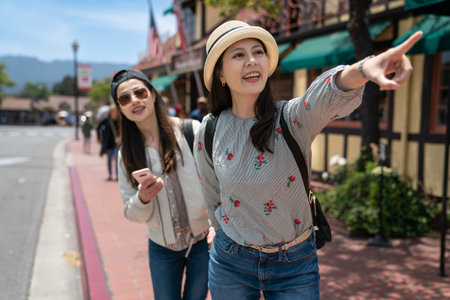 closeup portrait of happy asian taiwanese female visitor pulling friend's hand and looking at famous attraction with pointing gesture on the street in solvang California usaの写真素材