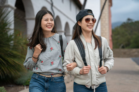 closeup portrait of two asian Taiwanese young women backpackers having fun touring around old mission santa Barbara in usa. they stand arm in arm and look into space with smiling faceの写真素材