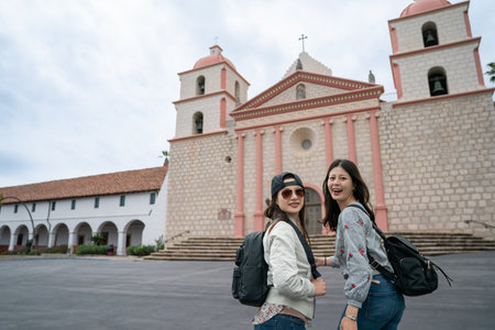 two asian Japanese female travelers turning to smile at camera during spring tour at old mission...