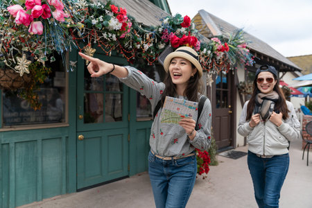 two happy asian chinese girl visitors heading for a famous attraction in Danish village with finger pointing gesture during their spring travel in solvang California usaの写真素材