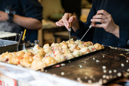 closeup cropped shot hands of chef using two takoyaki picks to turn octopus dumpling balls on pan at a food stall in Shinsekai area in Osaka Japanの写真素材
