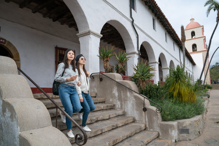 full length of two asian chinese female backpackers walking down stairs near the archway as while...