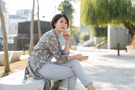 Asian girl sit at sidewalk during sunset at seaside. Cute young Japanese woman enjoy summer evening at river or sea looking at sun setting in water Kyoto Japan.の写真素材