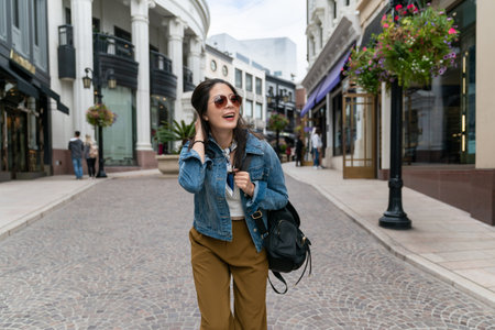 Cheerful asian woman in a jean jacket smiles sincerely outdoors. Happy lady laughs and walks in great mood outside.の写真素材
