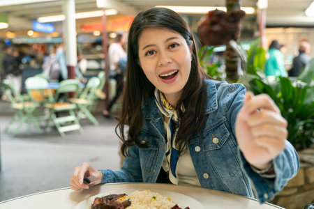 smiling girl facing camera is using knife to feed her son a piece of steak with fork. Enjoy a cozy...