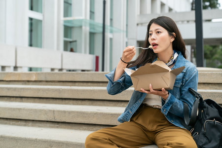 Korean international students girl enjoying food sitting on the outside stairs during lunch break in the Los Angelesの写真素材
