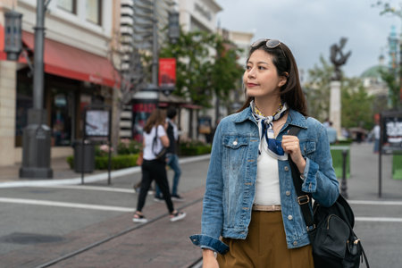 Asian Korean girl carrying a bag and wearing sunglasses on her head crossing the road in leisurely afternoon. real life conceptの写真素材