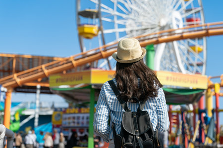 rear view of asian Taiwanese woman backpacker walking towards Ferris Wheel and other park rides in the amusement park.の写真素材