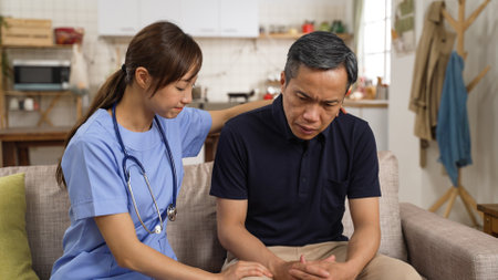 Asian female psychotherapist giving mental support to depressed elderly male patient. She taps his back gently while he is listening with head nodding at consultationの写真素材