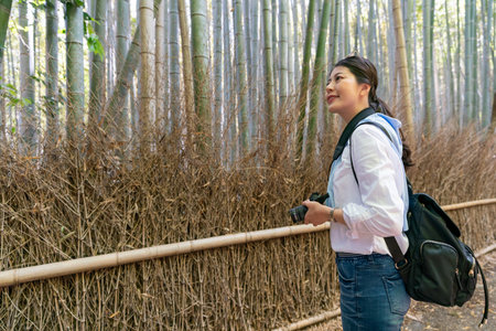happy asian Japanese woman tourist carrying camera and enjoying scenic view while looking at Arashiyama Bamboo Grove in Kyoto japan at springtimeの写真素材