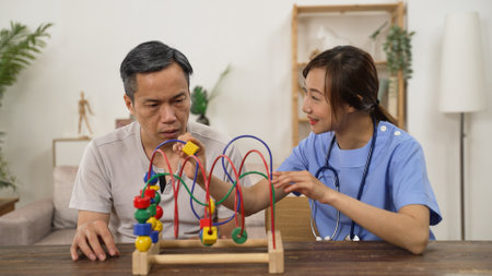 smiling asian Japanese female nurse giving instructions while helping older man go through physical therapy with bead maze. he tries to move the bead with injured hand slowlyの写真素材