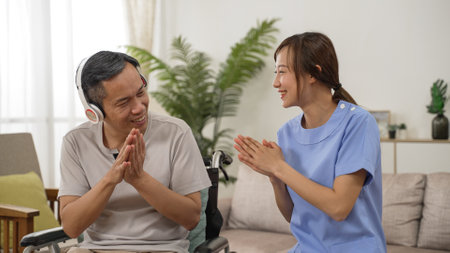 Asian Japanese senior man on wheelchair listening music from earphones and clapping hands with his nursing aide while having fun singing together during home visitの写真素材