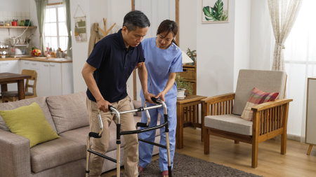asian Japanese senior stroke patient undergoing rehab exercise with a walker at home. the woman nursing aide assists him during home visitの写真素材