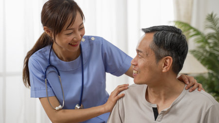 happy Japanese senior man having pleasant talk with friendly personal care attendant at home. the woman putting hands on his shoulders showing supportの写真素材