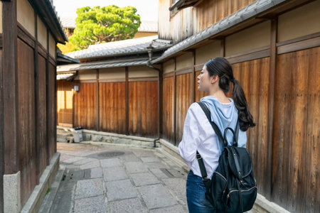 rear view of asian Chinese female backpacker looking at ancient traditional wooden buildings while exploring in stone paved Gion Ishibeikoji Lane in Kyoto japan.の写真素材
