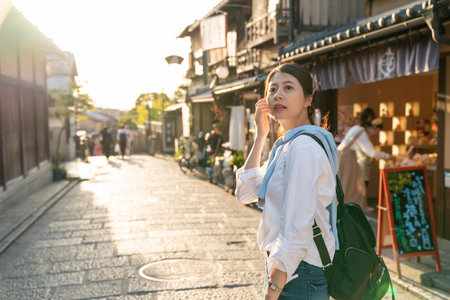 backlit curious asian Japanese woman visitor turning around to look at the surroundings while exploring Ninenzaka and Sannenzaka in Kyoto japan at duskの写真素材
