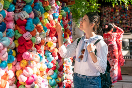 happy asian Japanese woman visitor enjoying looking at prayers written on Kukurizaru color ball ema at Yasaka Koshin-do temple in Kyoto japan. a girl wearing kimono is standing at backgroundの写真素材