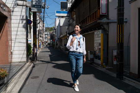 full length of amazed asian Taiwanese girl tourist having fun looking at old traditional Japanese houses while taking leisure walk on the street in downtown Kyoto japanの写真素材
