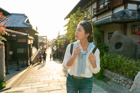 backlit confused asian korean girl visitor looking away into distance on a hill and thinking about where her location is while visiting Ninenzaka and Sannenzaka in Kyoto japan at twilightの写真素材