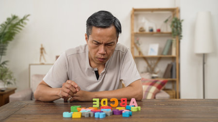 Korean male pensioner with Alzheimerâs disease trying to improve memory by doing rehab exercise for brain at home. He murmurs to himself while looking and counting the letter blocksの写真素材