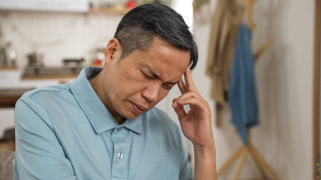 closeup of stressed asian elderly male worrying about problem alone at home. he props his head while thinking hard for solutionsの写真素材