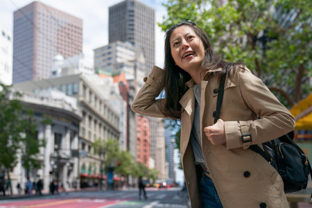 cheerful asian Taiwanese girl visitor having fun touring downtown san Francisco in California usa. she pushes hair back while waiting for bus at a stop on the streetの写真素材