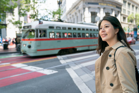 happy asian chinese business woman waiting on the street to take local bus to work in downtown San Francisco California usa. a green city bus passing by at backgroundの写真素材