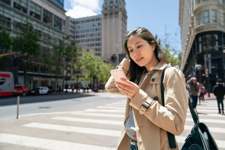 asian Japanese woman tourist holding hair and checking online guide on smartphone while exploring financial district on Market Street in san Francisco California usaの写真素材