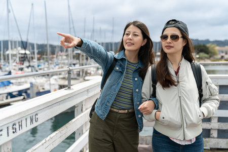 travel lifestyle and people on vacation in usa. asian woman visitor finger pointing at distance while walking arm in arm with her partner near fishing port Old Fisherman's Wharf in Californiaの写真素材