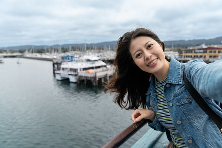 self portrait of happy asian woman visitor smiling at camera while taking selfie picture with boats near fishing port at Old Fisherman's Wharf in Monterey California usaの写真素材
