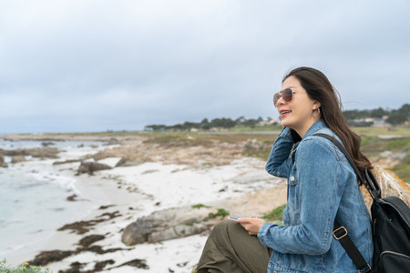 stylish asian Korean woman tourist feeling comfortable with cool sea wind while relaxing at coastal beach along pacific coast highway in California usaの写真素材