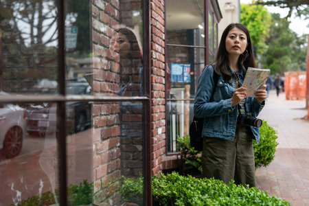 asian girl visitor looking into distance with a route map while traveling alone in Carmel by the sea. she is searching for the right way to go near a shop on the sidewalkの写真素材