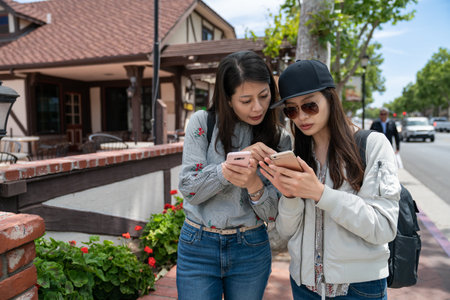 asian japanese woman visitor teaching her travel mate how to use navigation app on smartphone while they are touring downtown solvangin California usaの写真素材