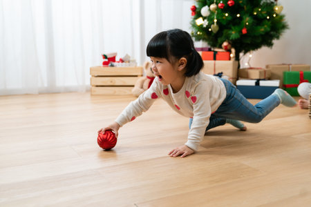 adorable asian little girl looking at empty area while having fun playing with a ball on the ground in a Christmas living room at home with daylight.の写真素材