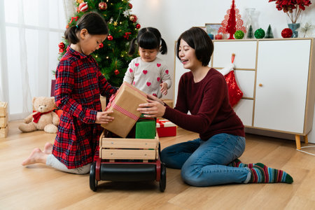 asian mother and her girls enjoying playing together with a toy cart and gifts in the living room decorated for Christmas at homeの写真素材